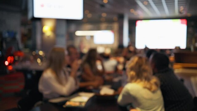 Defocused people sitting and having a chat at table in bar or pub