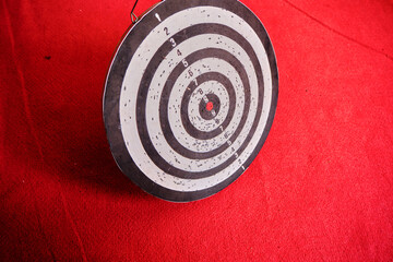 Used dart board standing on red carpet and its shadows.