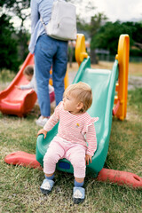 Fototapeta na wymiar Kid sits on a children's slide on a playground in a green park