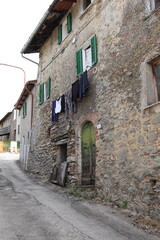 Fototapeta na wymiar Central Italy Village Street View with Old Stone Building, Green Wooden Door and Hanging Laundry