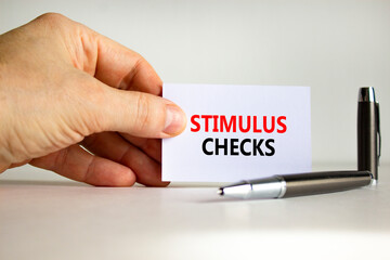 Stimulus checks symbol. White paper with words 'Stimulus checks' in businessman hand, metallic pen. Beautiful white background. Business, stimulus checks concept. Copy space.
