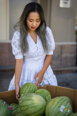 Young petite asian woman in summer dress shopping for melons