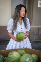 Young petite asian woman in summer dress shopping for melons