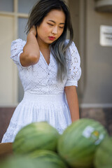 Young petite asian woman in summer dress shopping for melons