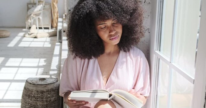 A young mixed race woman is carefully reading an interesting book, a fiction, a novel, thinking about what he was reading. A quiet day at home without electronic gadgets or mobile phones.