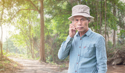 An elderly man uses a smartphone in the forest.