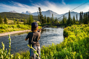 A young child casting his fishing rod into the Crossest River with a Rocky mountain backdrop in Southern Alberta Canada.