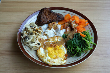A traditional Javanese dish called pecel, consisting of spinach, sprouts, carrots, fried eggs, and peanut brittle         