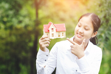 Fototapeta na wymiar Smiling young girl holding mini house. Real estate agent selling home concept
