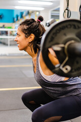 Fototapeta na wymiar young latin woman doing a barbell back squat. , with weight, smiling. Vertical photo.