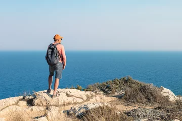 Gordijnen Man traveling with backpack hiking in mountains and looking on sea landscape. Active healthy lifestyle adventure journey vacations. © Sergey