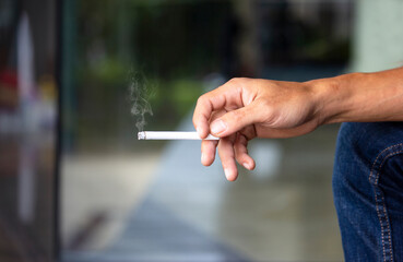 Man holding smoking a cigarette in hand. Cigarette smoke spread. dark background. Smoking causes cancer and harms others.
