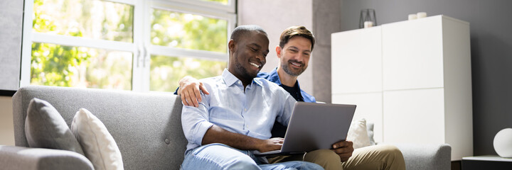 Gay Couple Using Computer For Video Conference On Sofa