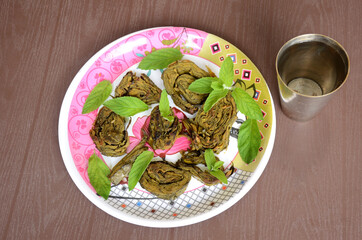 closeup the fried arabic leaves food with green mint in the plate and water brass glass over out of focus brown background.