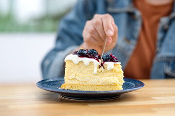 Closeup image of a woman eating blueberry cheesecake with spoon