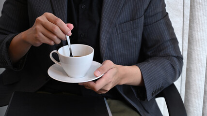 Cropped shot businessman in suit siting on office chair and holding cup of coffee.