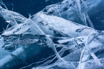 Beautiful cracks in the thick clear ice of the lake. Blue transparent ice with white cracks. Horizontal.