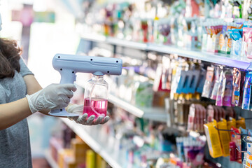close up hand of staff wearing gloves using electric Alcohol Nano Spray Gun Handhold Blue Light Disinfectant Spray. prevent infection Covid-19 in the shop. concept healthcar