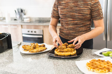 unrecognizable woman plating cereal battered fried chicken over waffles and syrup