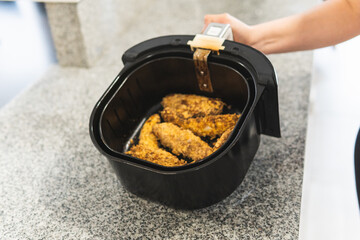 Close-up of woman's hand using an air fryer with fried chicken in cereal batter