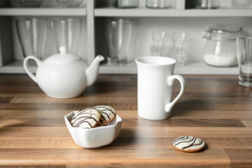 White tea cup, teapot and cookies in white bowl on the countertop of a Scandinavian-style kitchen, teatime and breakfast concept