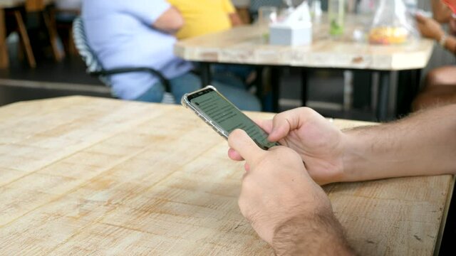 Man hands with mobile phone serf internet and reading news sitting in cafe with peoples on background. Male watching on screen of his smartphone. 4k