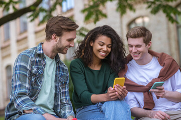 Fototapeta premium Group of young people sitting on the behcn and holding smartphones in hands