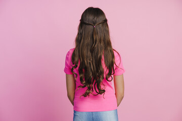 Back view of a girl with long hair, beautiful hairstyle on a pink wall background. Cute little girl...