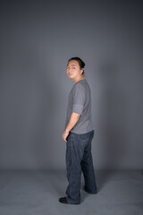 Asian long hair friendly and positive man is posting and standing in front of gray background with studio light.