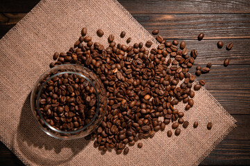 coffee beans and transparent jar on a dark brown wooden table covered with burlap