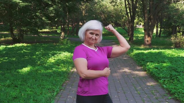 Mature woman in sportswear shows her biceps and muscles, showing her strength and self-confidence. Elderly people healthcare,  and healthy lifestyle concept.