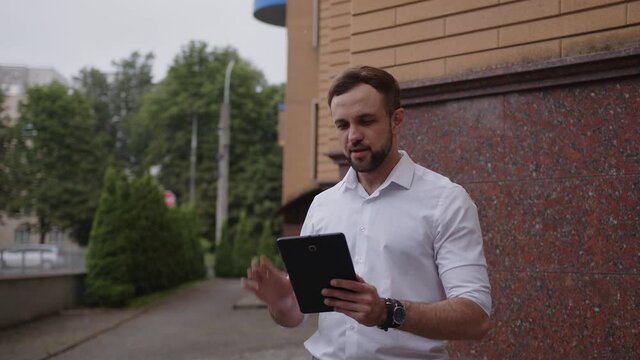 Young worker talks outdoor on his black tablet