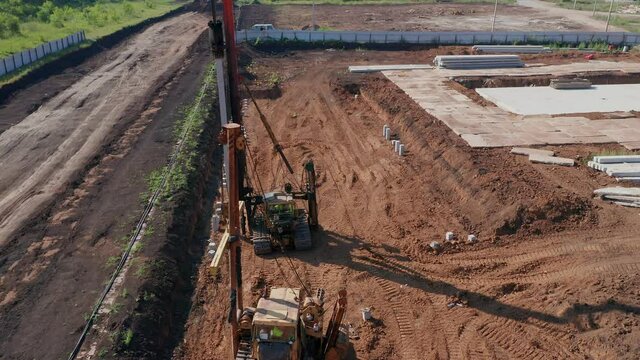 View from above of the fenced construction site. Two heavy pile-driving machines on the site covered with brown sand. Machinery and equipment. High quality. 4k footage.