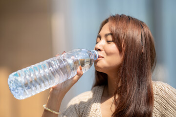 Asian Woman drinks big bottle water in outdoor green bokeh tree background.