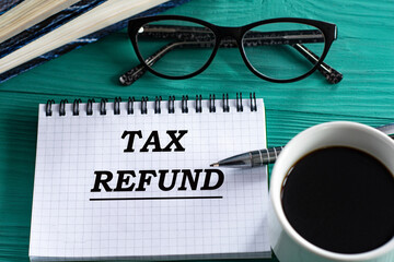 TAX REFUND - words in a notepad on a wooden green background with a calculator, pen and glasses