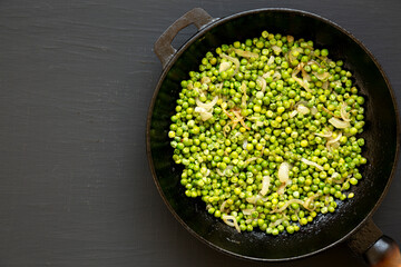 Homemade Sauteed Green Peas in a cast-iron pan, top view. Flat lay, overhead, from above. Copy space.