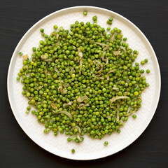 Fototapeta premium Homemade Sauteed Green Peas on a plate on a black surface, top view. Flat lay, overhead, from above.