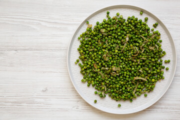 Homemade Sauteed Green Peas on a plate on a white wooden surface, top view. Flat lay, overhead, from above. Copy space.