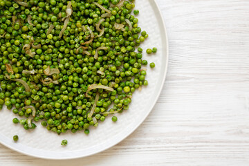 Homemade Sauteed Green Peas on a plate on a white wooden background, top view. Flat lay, overhead, from above.
