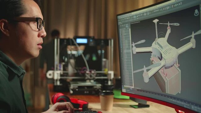 Close Up Of Frustrated Asian Engineer Working On Personal Computer And 3D Printer, Screen Shows Cad Software With 3D Prototype Of Drone Delivery
