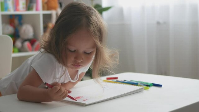 Cute toddler girl draws with felt-tip pens. Portrait of toddler girl at home.