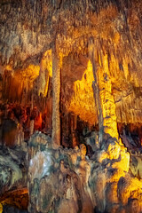 Natural stone pattern of mineral formations underground. Many stalactites and stalagmites illuminated by yellow light in Damlatas cave (Alanya, Turkey), vertical