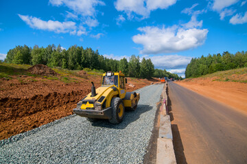 yellow tractor roller compacts stones against the background of a new road