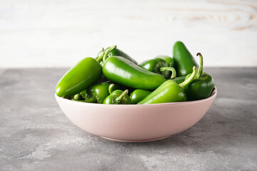 Green jalapeno peppers in a pink plate on a grey background.