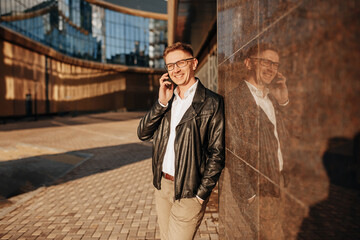 Handsome man with glasses with a smartphone on the street of a big city. Businessman talking on the phone on urban background