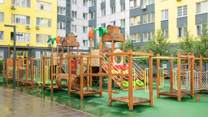 Fototapeta na wymiar A courtyard of high-rise buildings with a modern and large playground made of wood and plastic on a rainy summer day without people. Empty outdoor playground. A place for children's games and sports.