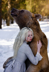 Beautiful white haired girl in vintage dress hugging brown bear in winter forest