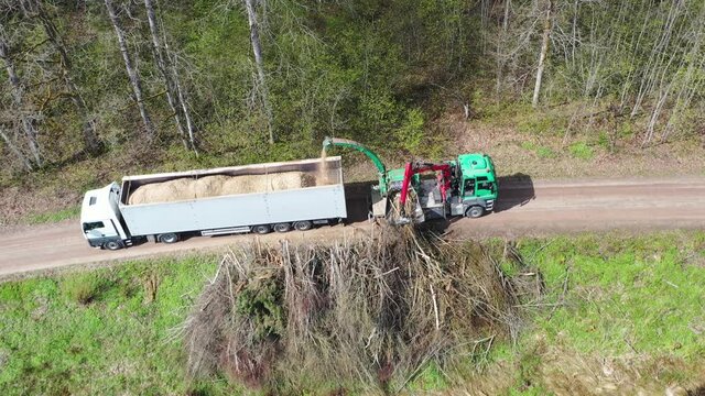 Aerial shot of wood chipper blowing shredded wood into back of a truck. Forest background