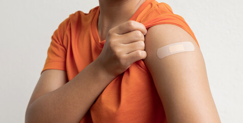 Asian woman shows plaster on her shoulder after being vaccinated against Covid-19. Coronavirus vaccination campaign concept - obrazy, fototapety, plakaty