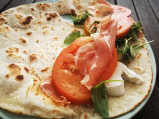 Piadina Romagnola with mozzarella cheese, tomatoes, ham and rocket salad on a cutting board.